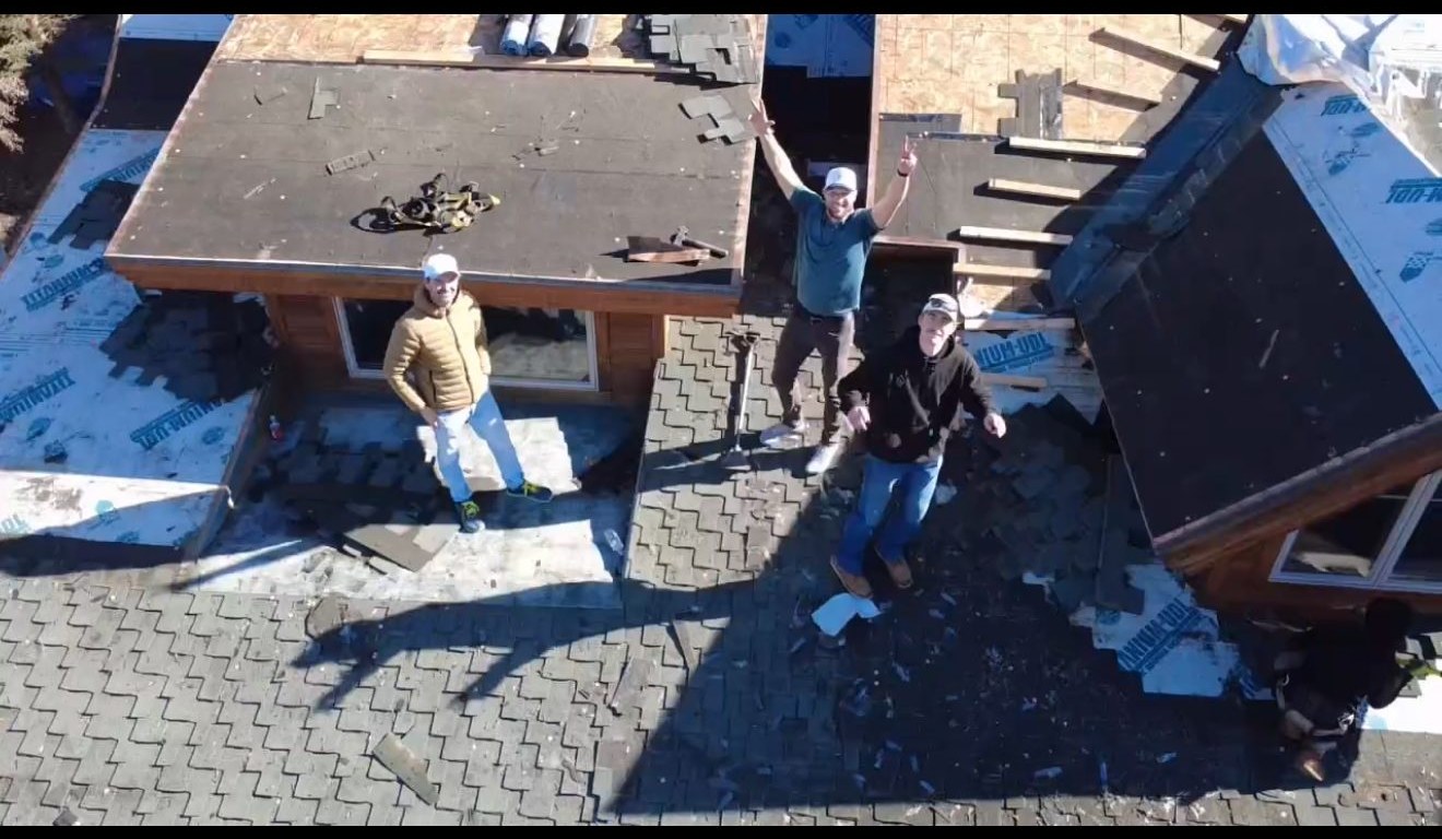 Crew working on roof tear-off waving at drone camera